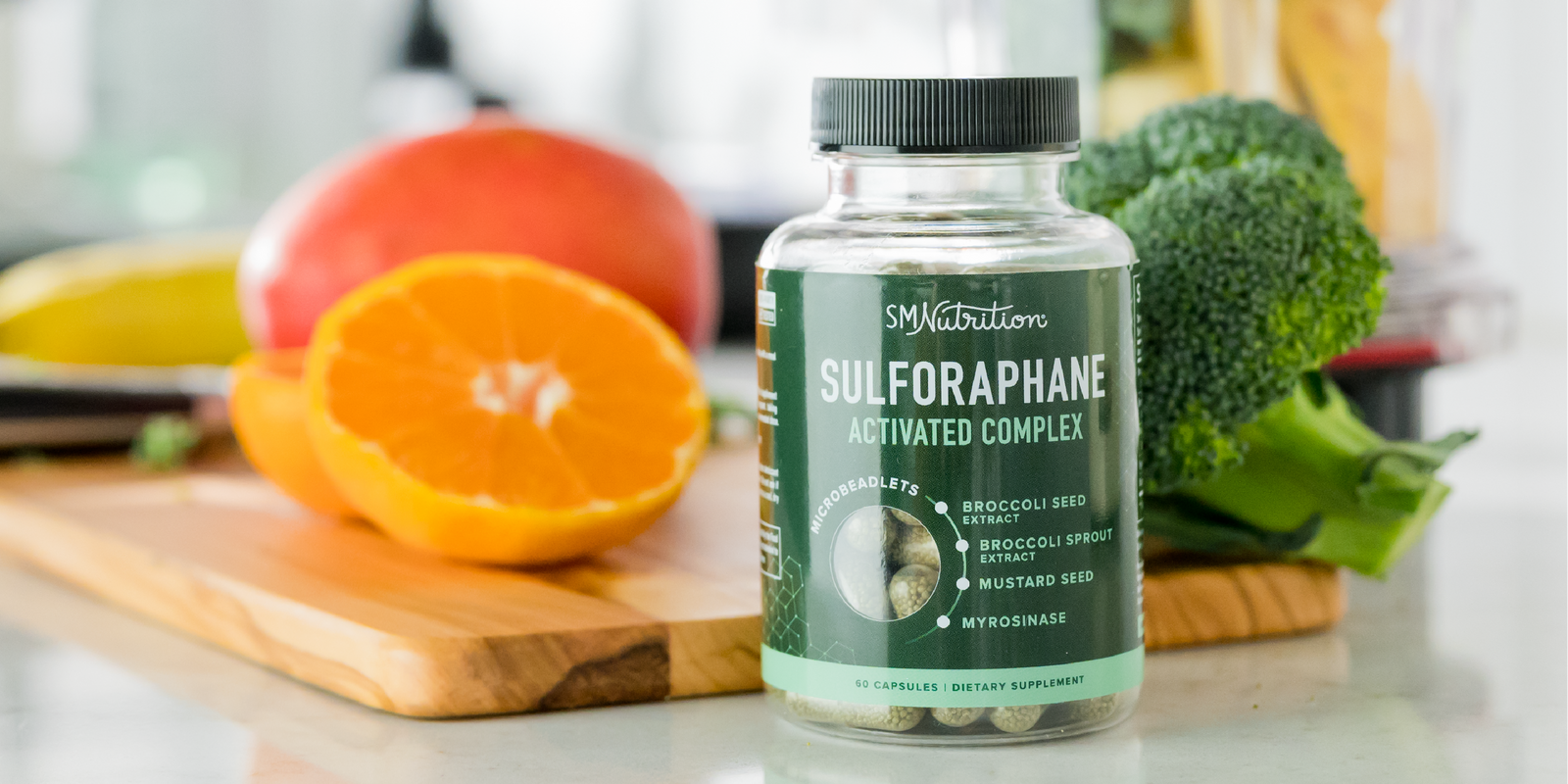 a bottle of Sulforaphane supplements by SM Nutrition sits on a kitchen counter in front of a wooden cutting board with fruits and vegetables