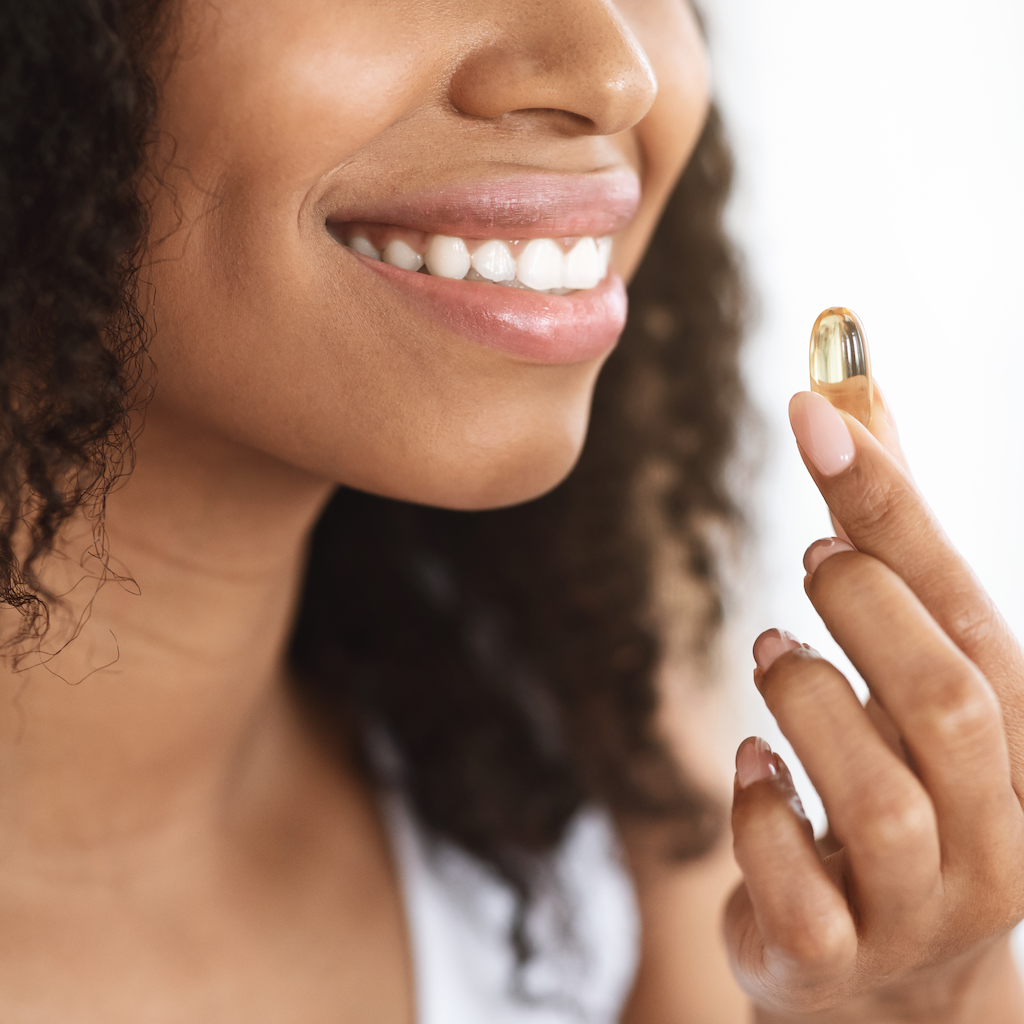 closeup of a woman holding a fish oil capsule close to her mouth, as if about to swallow it